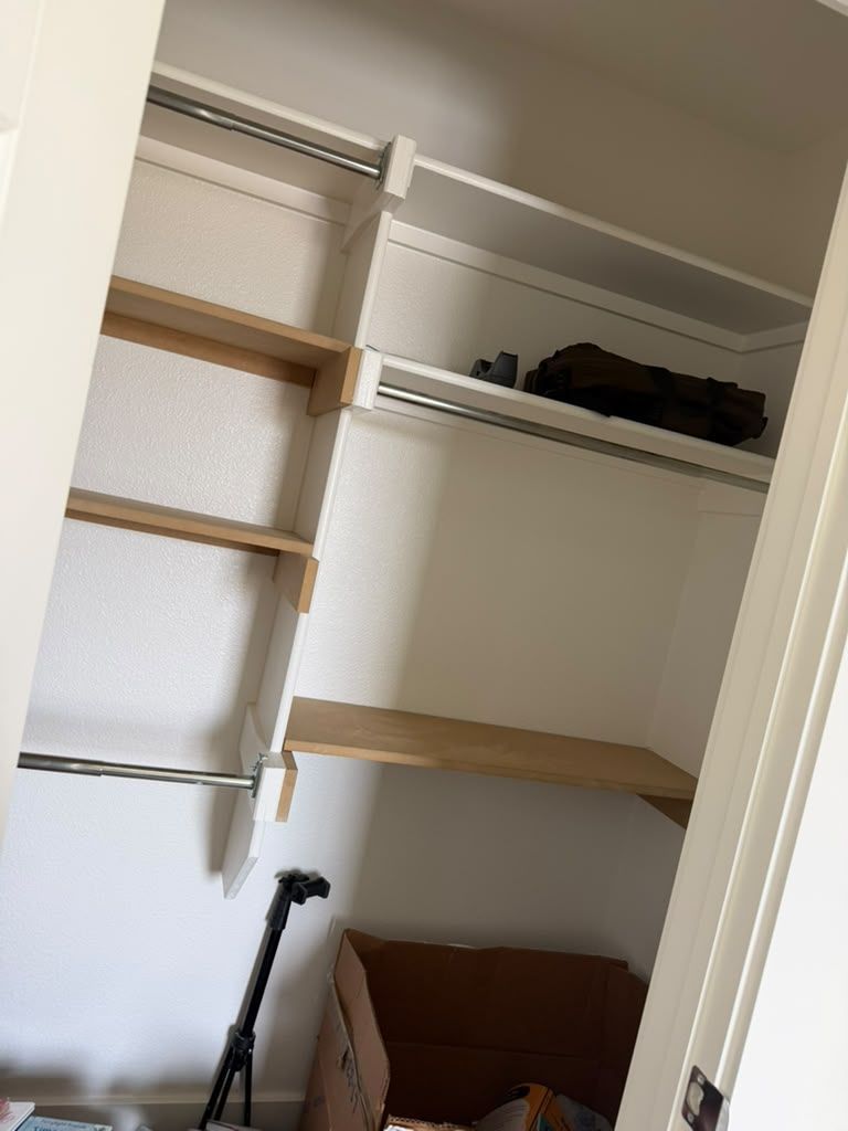 Open closet with empty shelves, hanging rods, and a box on the floor; a tripod stands inside.