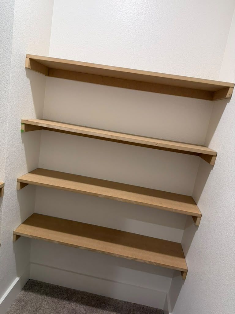Empty wall-mounted wooden shelves in a corner above a carpeted floor.
