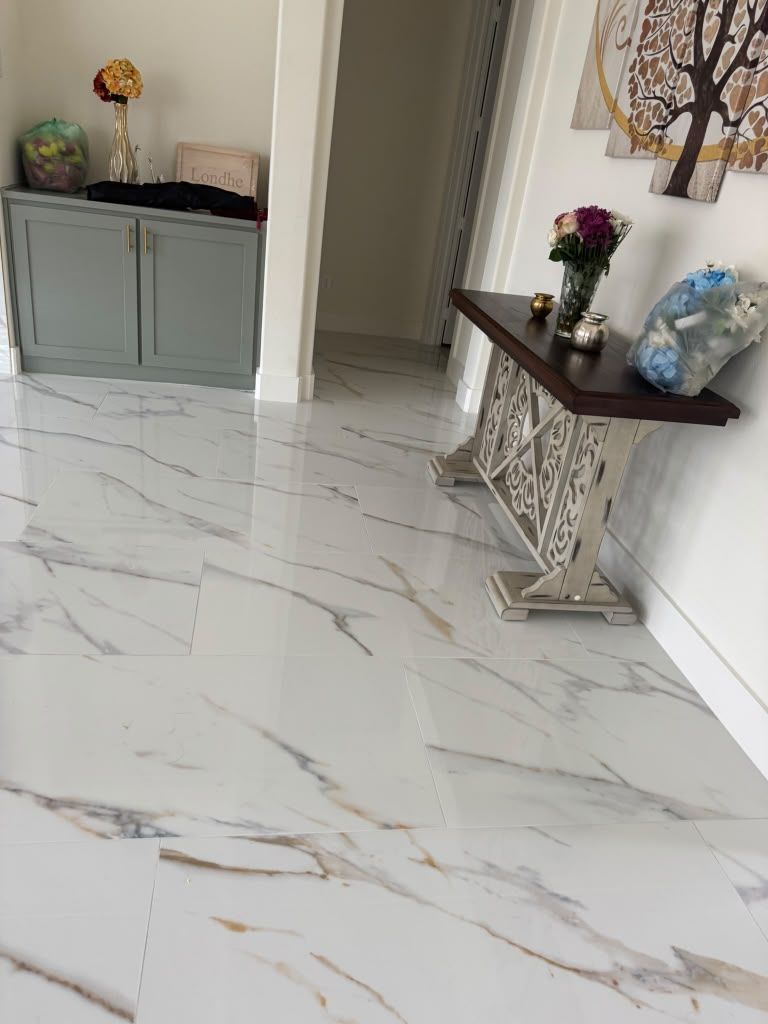Bright marble-tile hallway with a gray cabinet and decorative console table with flowers and plants.