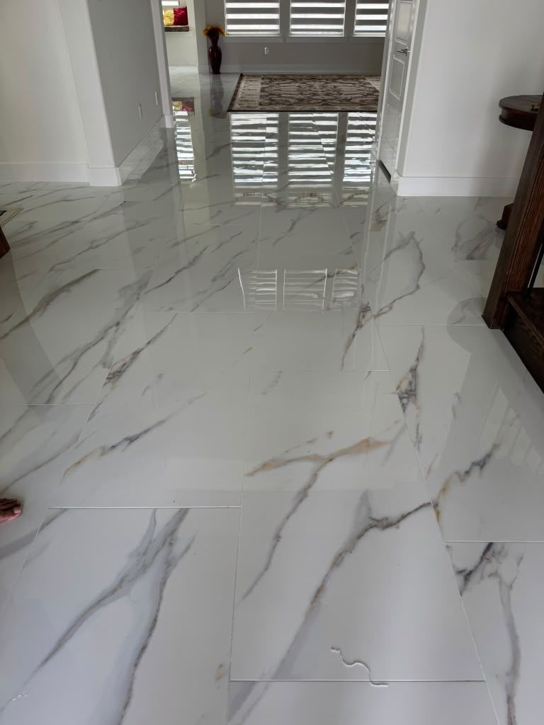 Glossy white marble floor with gray veining in a bright hallway, reflecting a doorway and furniture nearby