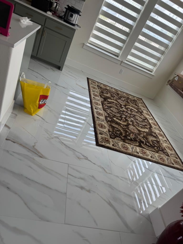 Bright tiled room with a yellow bucket, patterned rug, and white shuttered windows reflecting light.