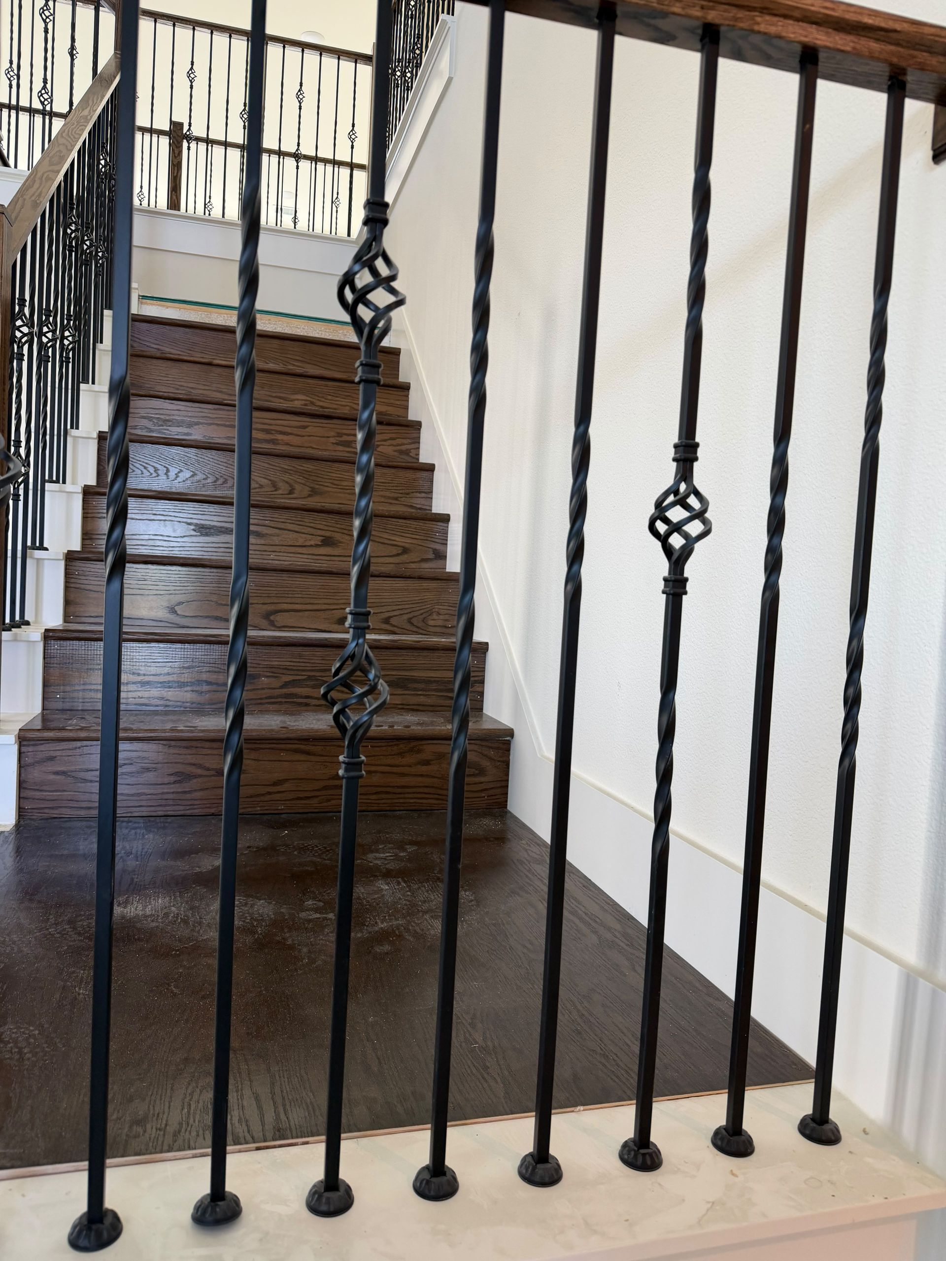 Black iron stair railing in front of a wooden staircase and beige hallway wall.