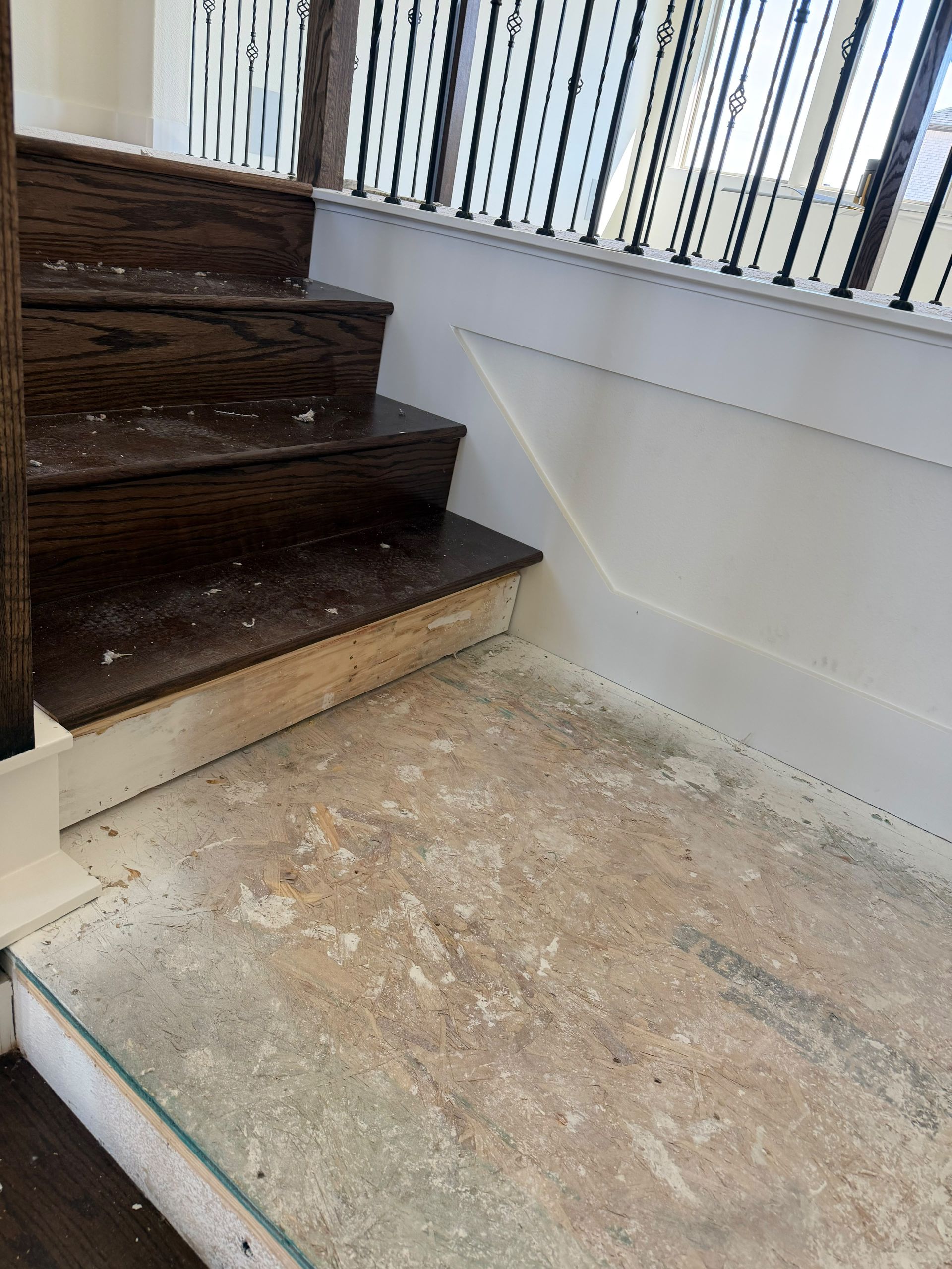 Staircase with dark wood steps beside a dusty concrete landing and white wall with railing shadows