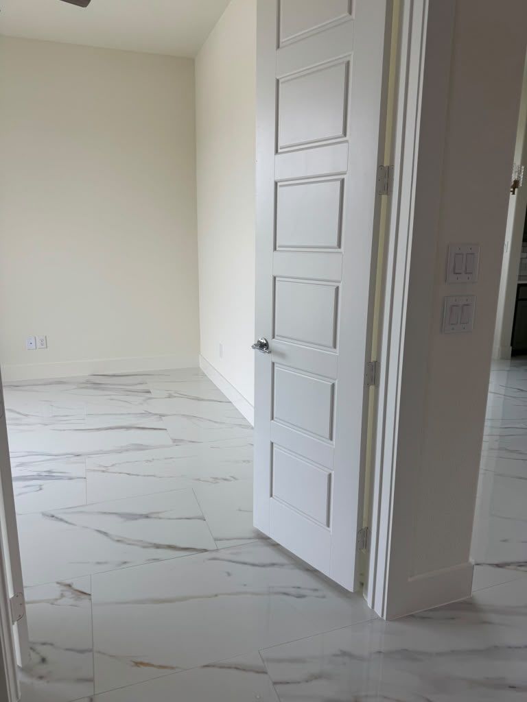 Empty white room with marble tile floor and a paneled white door ajar