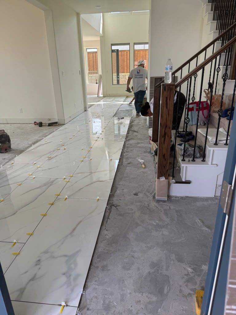 Hallway with tiled floor under construction; worker stands near a staircase and tools.