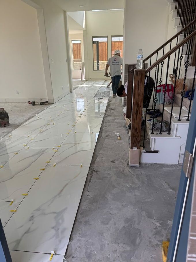 Renovation hallway with marble floor tiles, staircase railing, and a worker cleaning near the far wall.