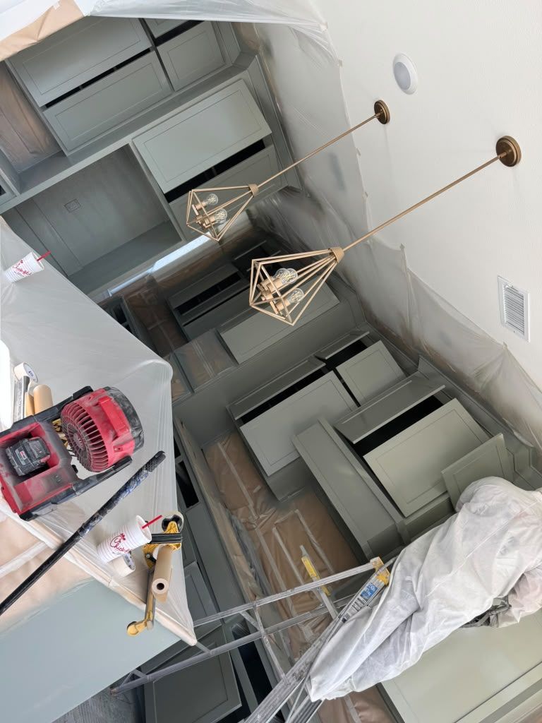 Renovated kitchen with white cabinets, hanging pendant lights, and a countertop covered in tools and plastic sheeting