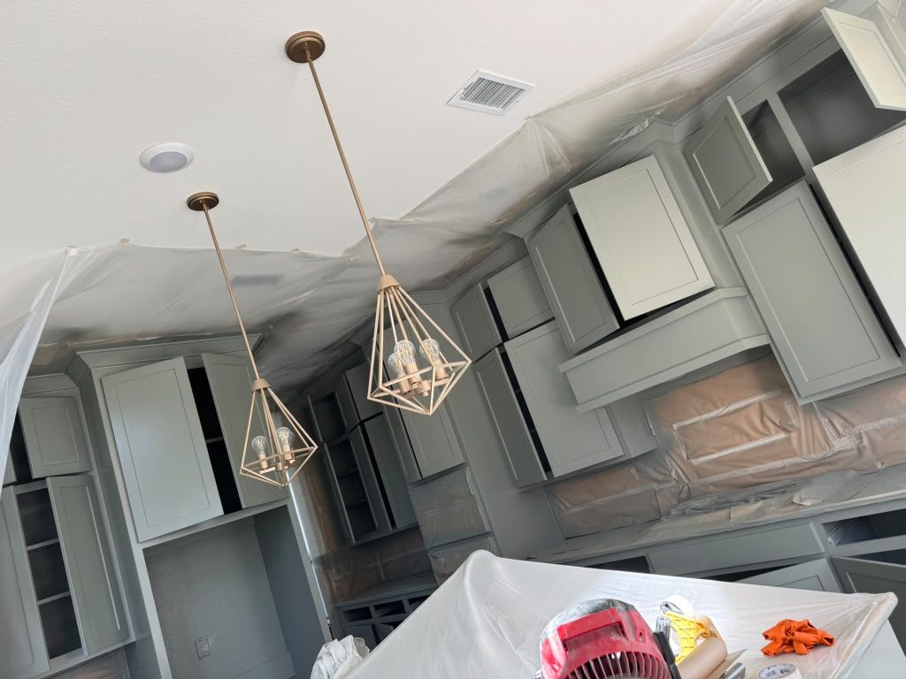 Damaged kitchen with loose ceiling tiles, hanging light fixtures, and exposed insulation above cabinets