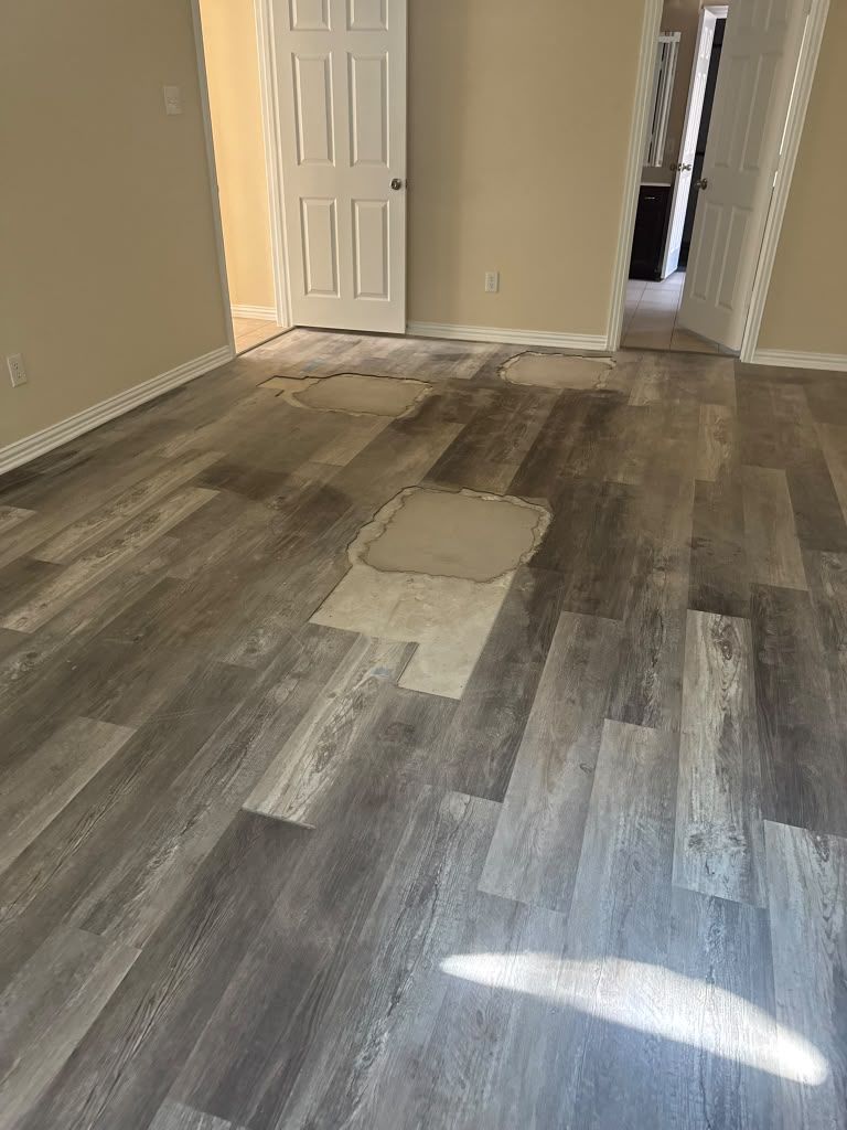 Empty room with gray wood-look flooring, tan walls, and a white door in the back.