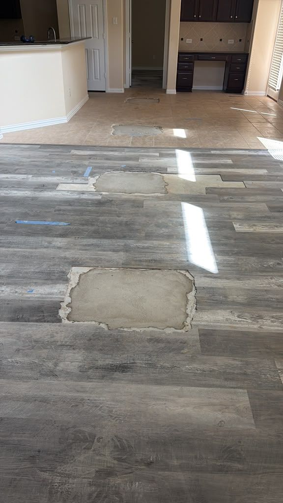 Damaged wood-look floor with a patched section in an empty room leading to a hallway