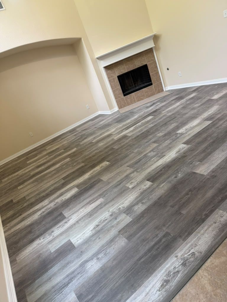 Empty beige living room with gray wood-look flooring and a fireplace
