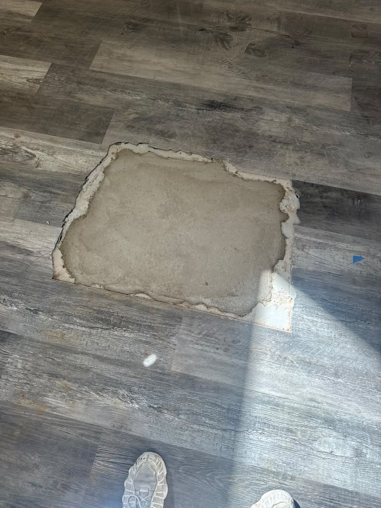 Damaged vinyl floor with a square patch and a small hole below, lit by sunlight.