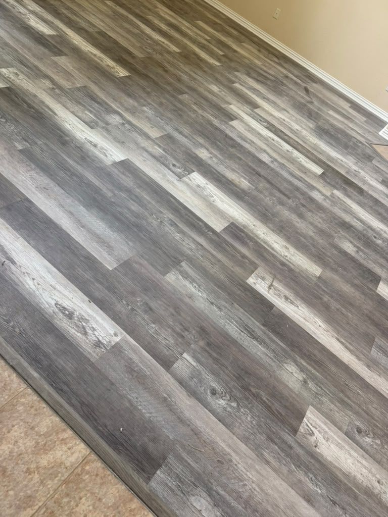 Gray wood-look flooring beside beige tile near a wall