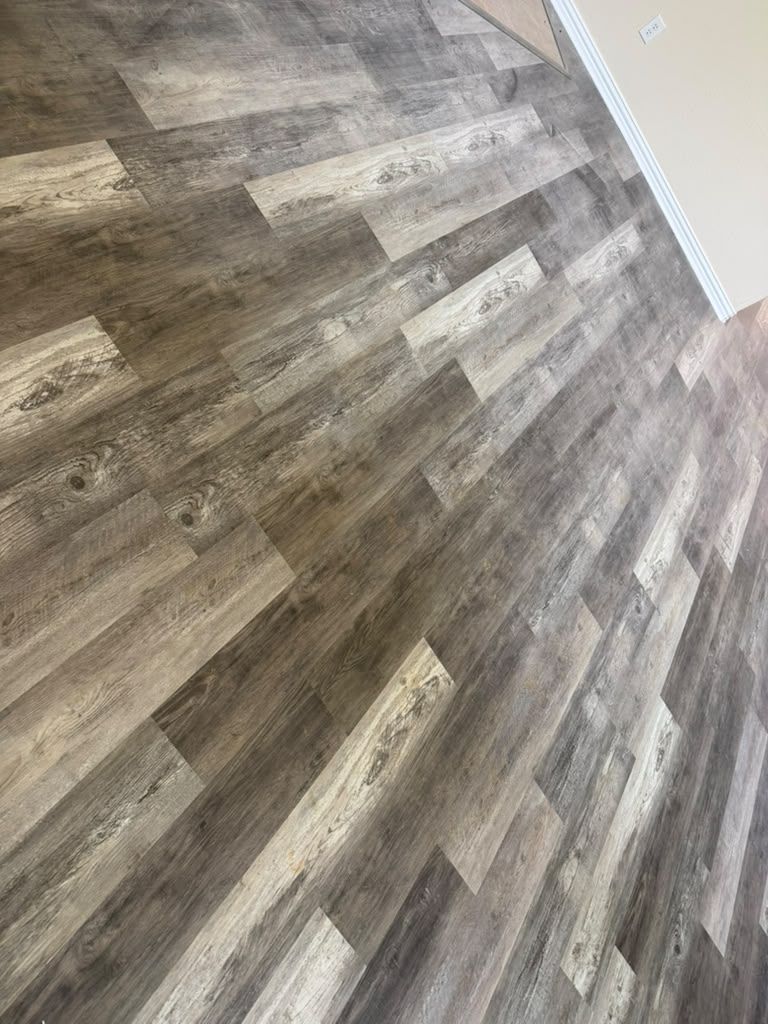 Empty room with gray-brown wood-look flooring and white baseboards, viewed at an angle.