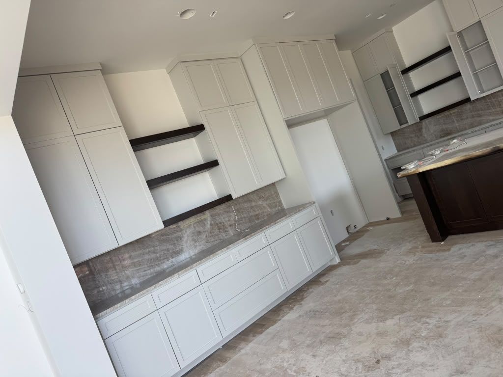 Bright unfinished kitchen with white cabinets, gray backsplash, and dark open shelves.