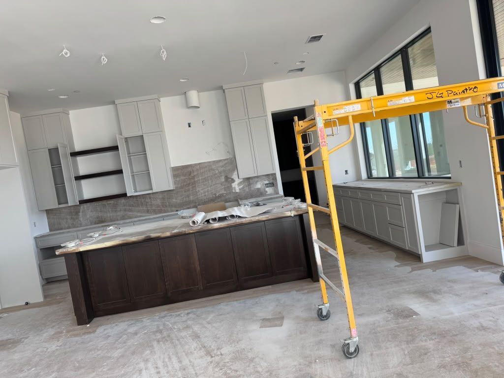 Bright unfinished kitchen with dark island, white cabinets, and yellow construction scaffold