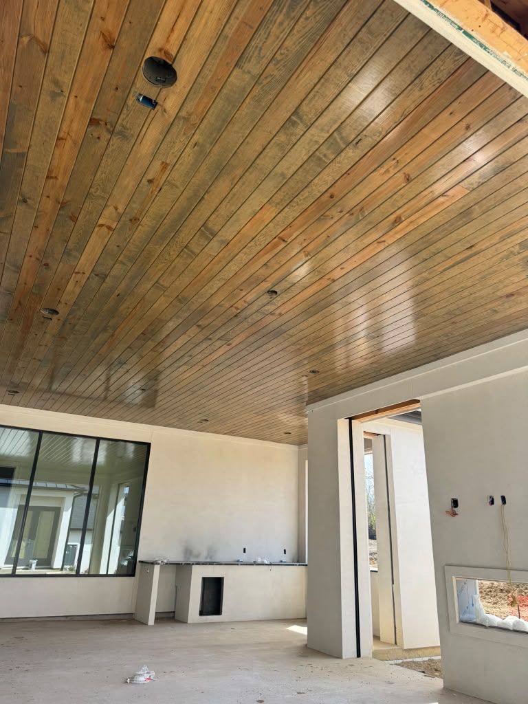 Empty room under construction with wood-paneled ceiling, white walls, and large windows.