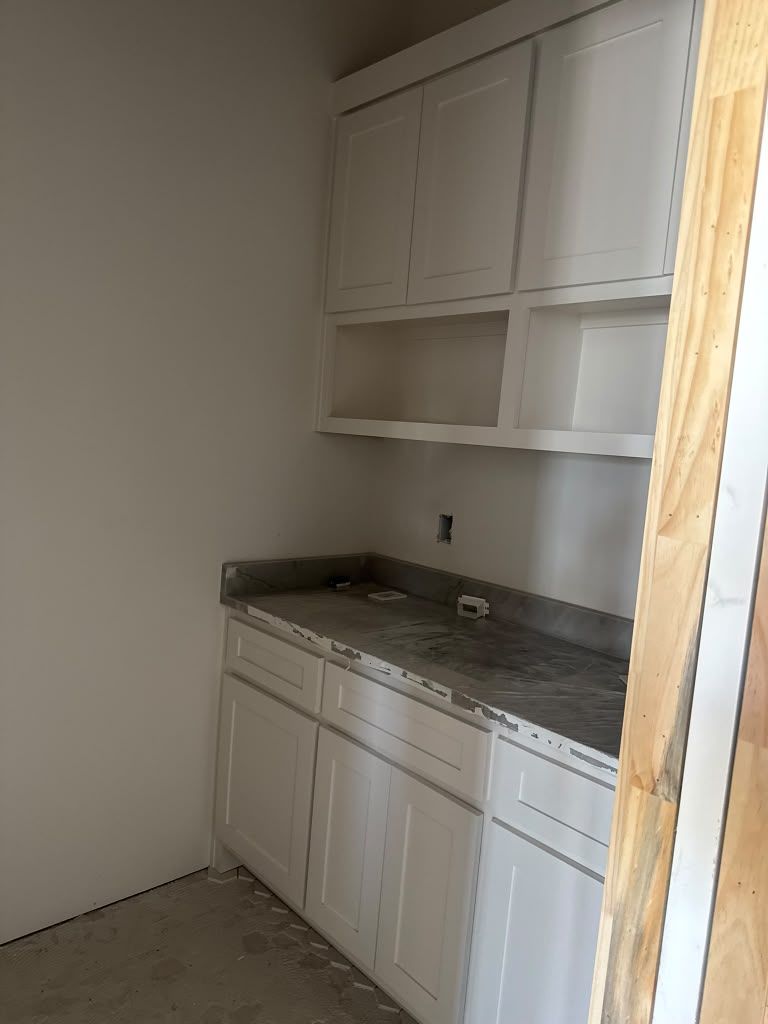 Small kitchen with white cabinets, gray countertop, and unfinished floor under renovation