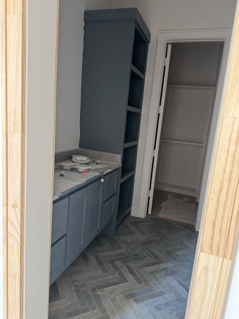 Small kitchen alcove with gray cabinets, open shelving, and a doorway to a closet on herringbone flooring