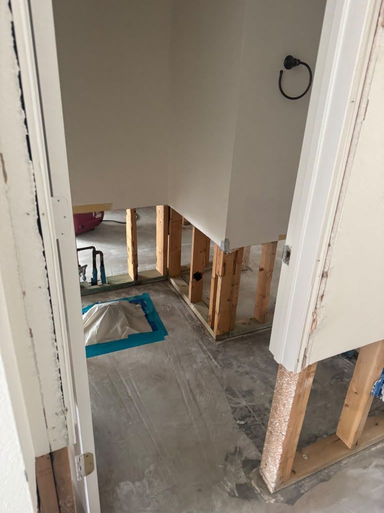 Interior room under renovation with exposed wall studs and a small blue-framed floor opening