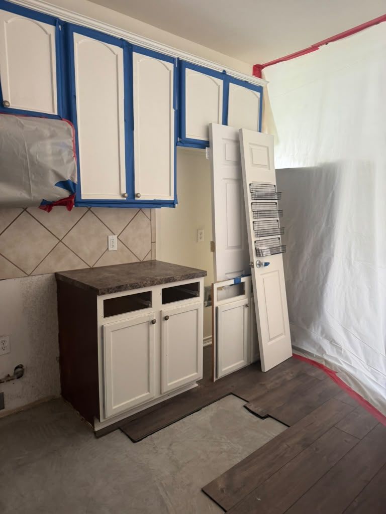 Kitchen renovation with blue-trimmed cabinets, tile backsplash, countertop, and protective plastic sheeting