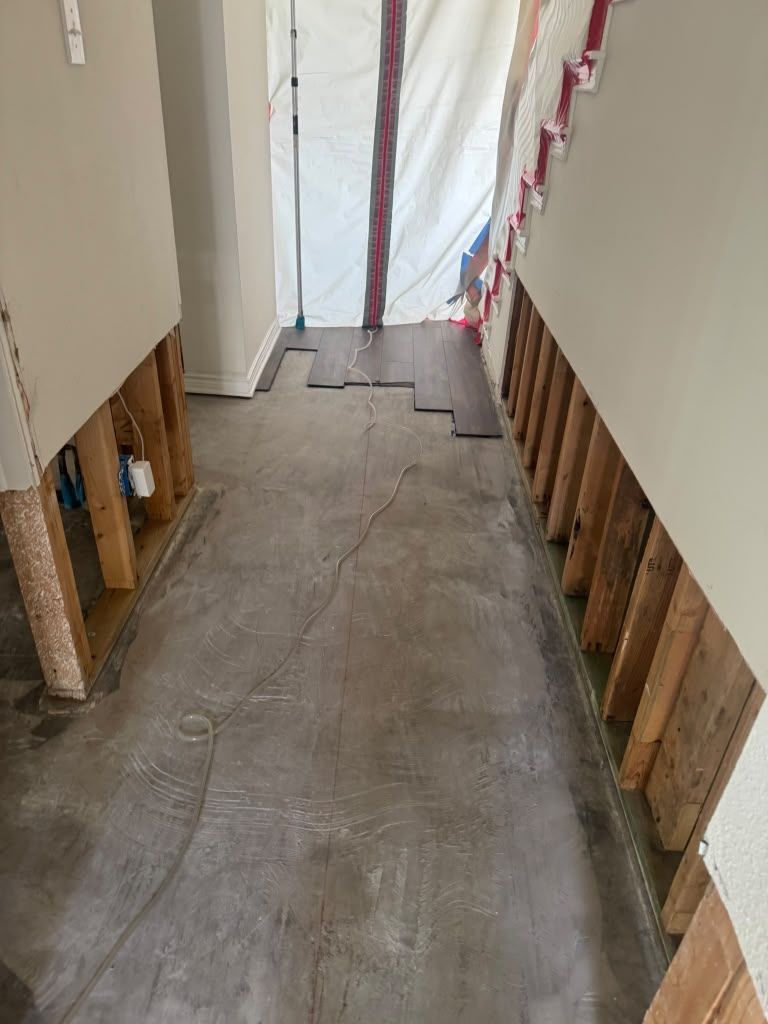 Narrow hallway under construction with exposed wall studs, unfinished floor, and plastic sheeting at the end.