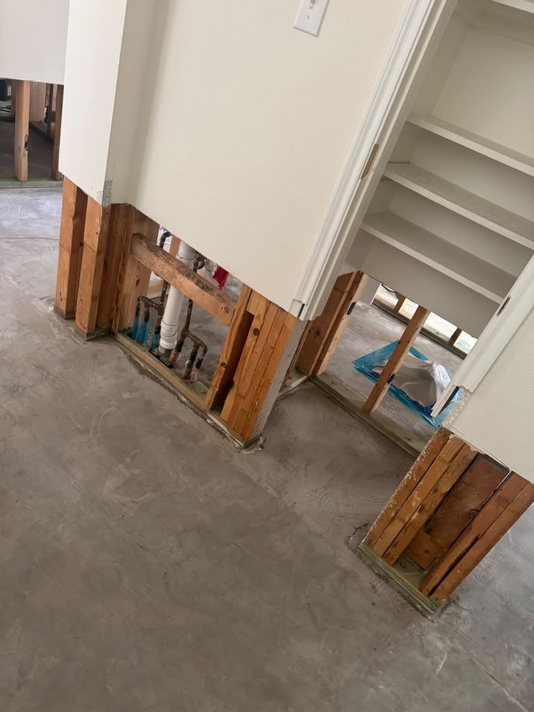 Damaged wall base with exposed studs and insulation in an unfinished interior hallway