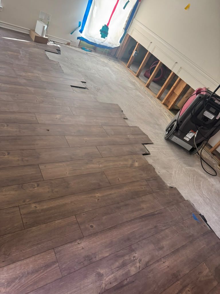 Partially installed dark wood flooring in a room under renovation, with exposed wall framing and tools nearby
