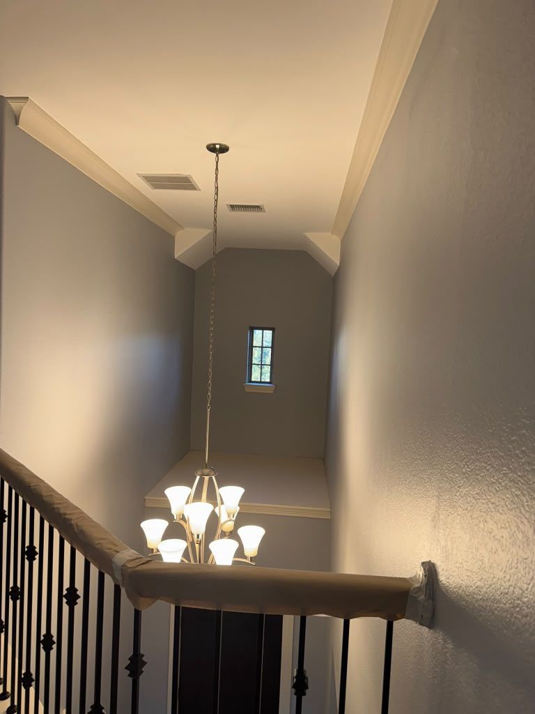 Stairwell hallway with gray walls, ceiling light, and a chandelier hanging below a landing window