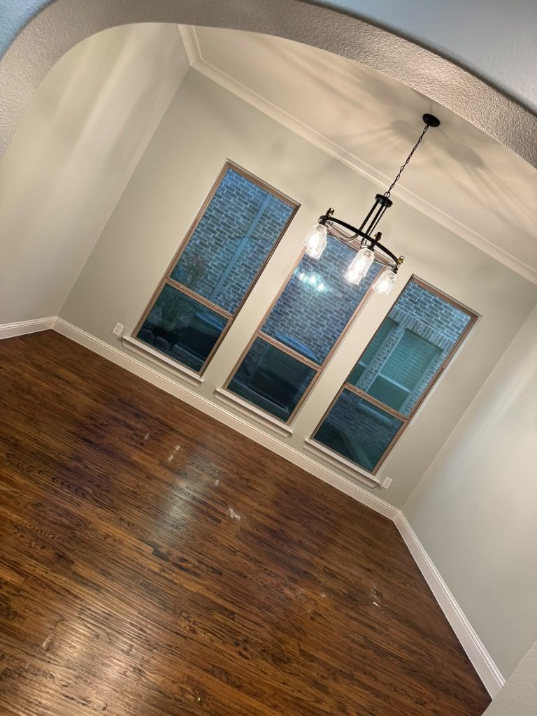 Empty dining room with dark hardwood floors, white walls, and three blue-tinted windows under a hanging light fixture