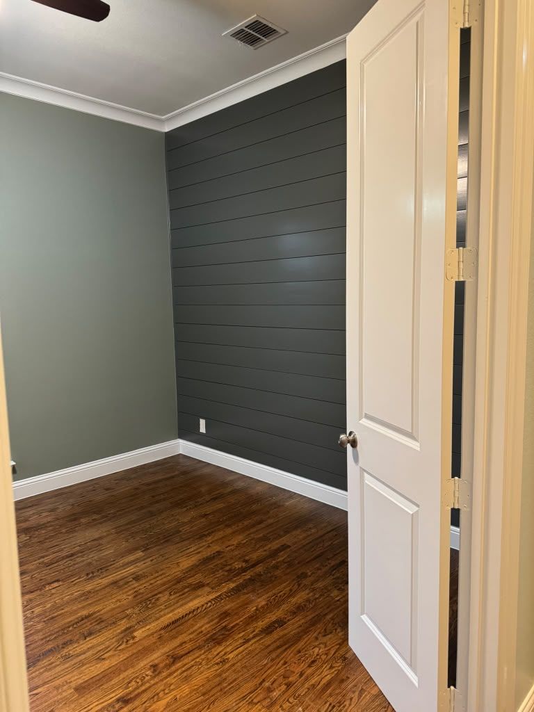Empty room with wood floor, gray walls, and an open white door.