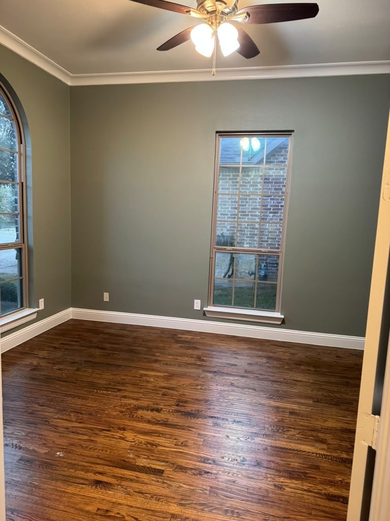 Empty room with dark wood floors, gray walls, ceiling fan, and two windows with blinds.