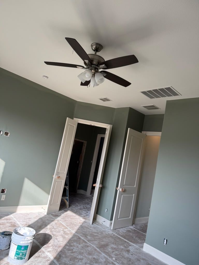 Empty room with gray walls, tiled floor, ceiling fan, open doorway, and a paint bucket on the floor.
