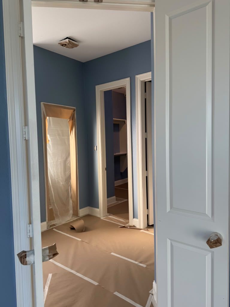 Blue hallway with open white doors, a leaning mirror, and a plastic-covered floor under renovation