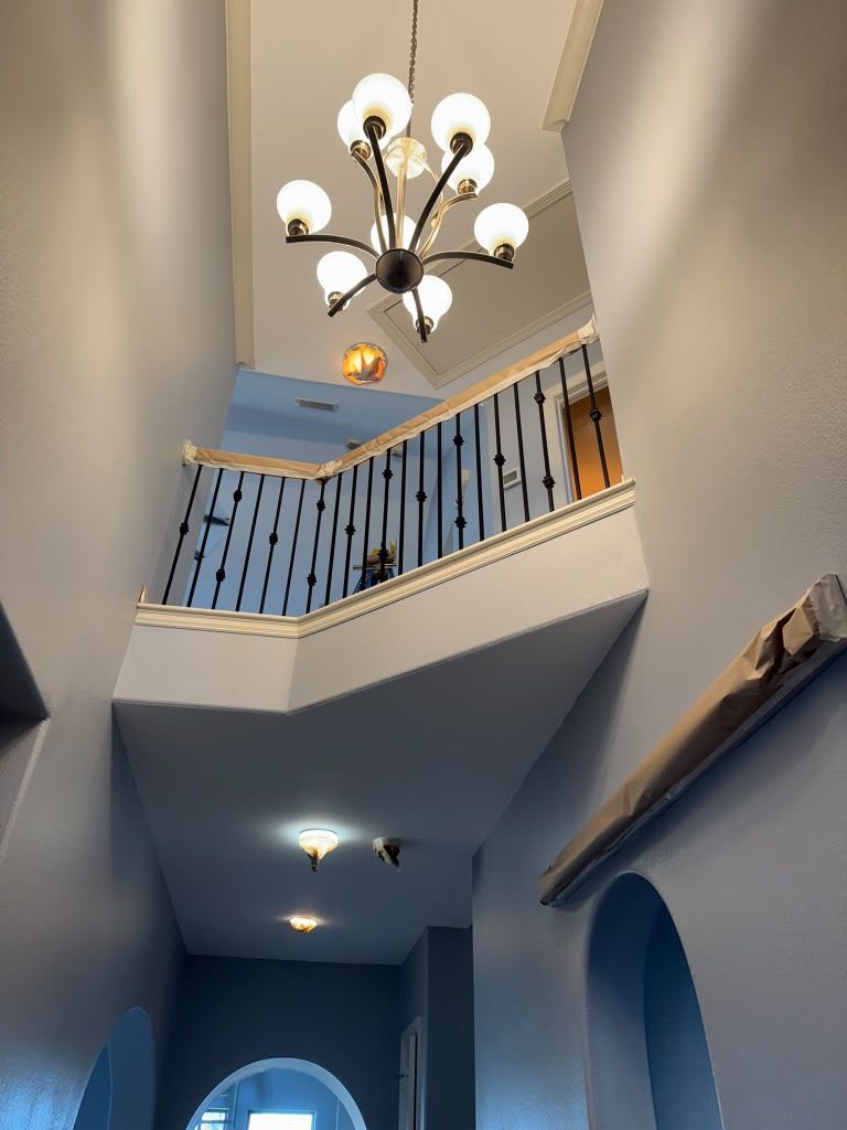 Hallway with a high ceiling, chandelier, and blue stair railing overlooking an archway below