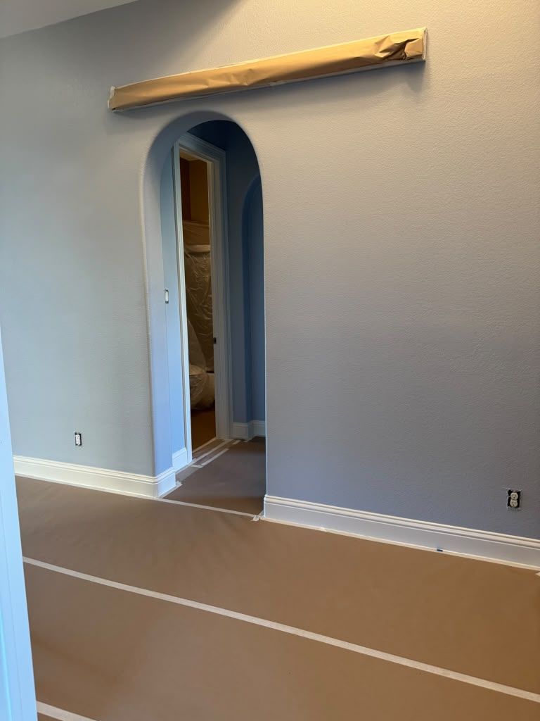 Empty room with a blue arched doorway and a mounted shelf above a brown carpeted floor.