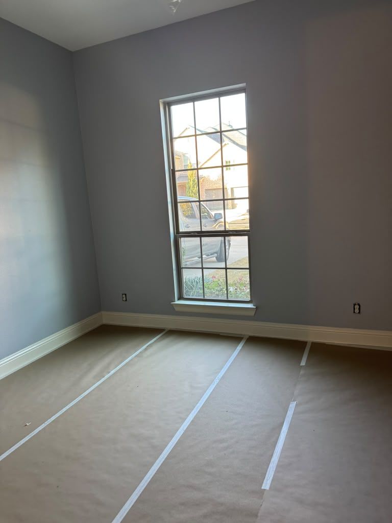 Empty gray room with a tall window and taped floor markings under construction.