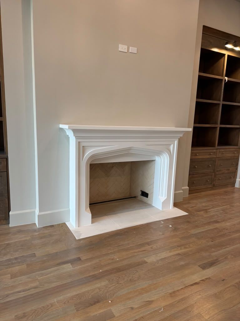 White decorative fireplace mantel in a room with hardwood floors and built-in shelving.