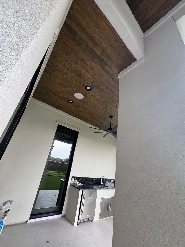 Modern indoor patio with wood ceiling, ceiling fan, and large open doorway