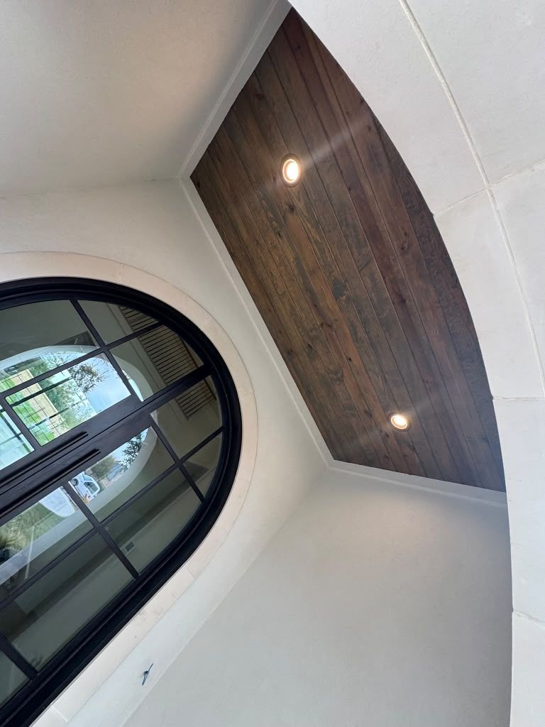 Modern interior ceiling with arched window, white walls, and a wood accent panel with lights.