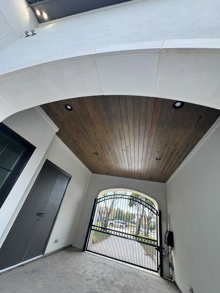 Covered entryway with white walls, wood ceiling, and black gate opening to a sunlit courtyard