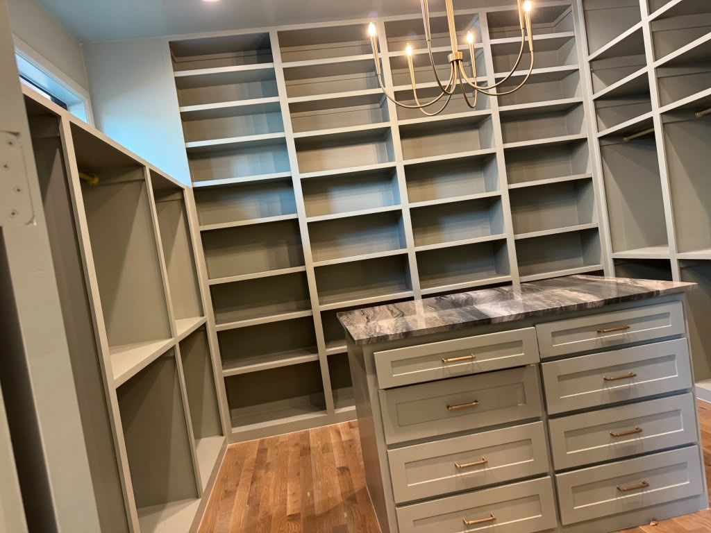 Custom walk-in closet with built-in shelves, hanging space, drawers, and a central island with chandelier lighting.