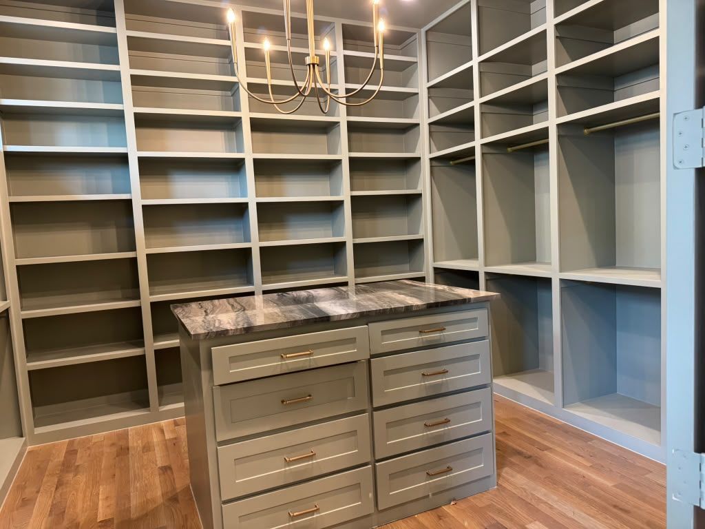 Walk-in closet with gray built-in shelving and a central drawer island on wood flooring
