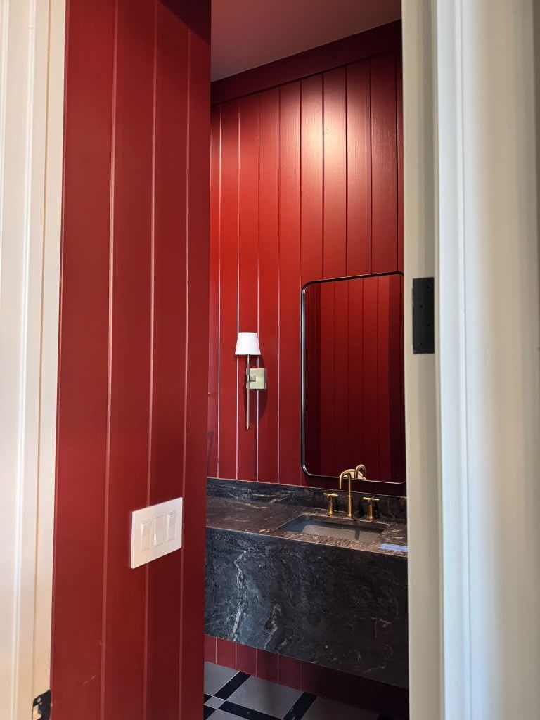 Red bathroom with black marble sink vanity and mirror, viewed through a doorway.