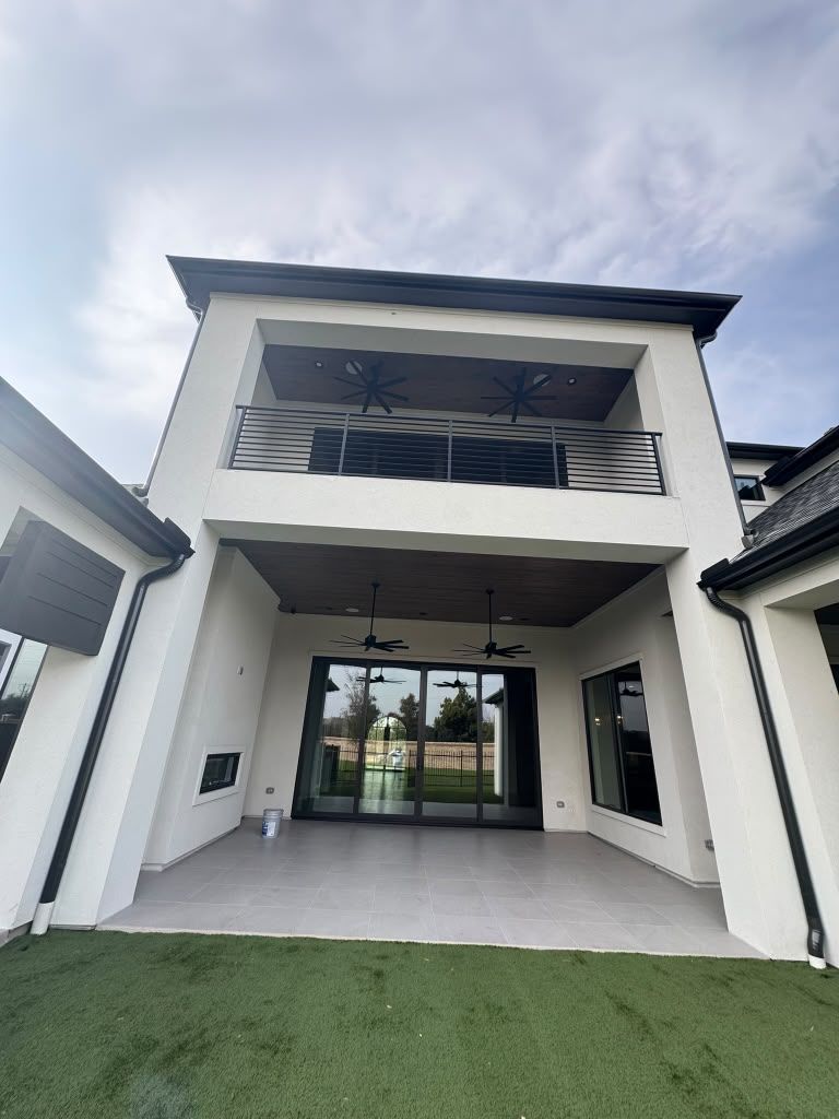 Modern white two-story house with a covered entry, balcony, and green turf front yard