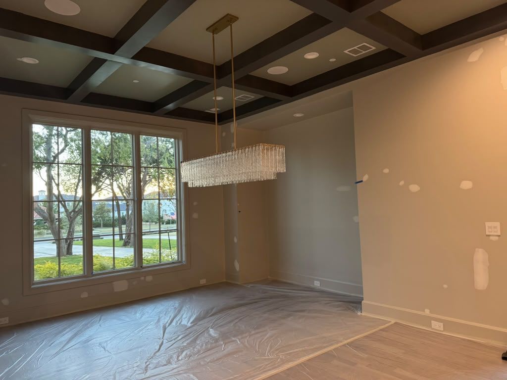 Empty modern dining room with large windows, coffered ceiling, and hanging chandelier under renovation