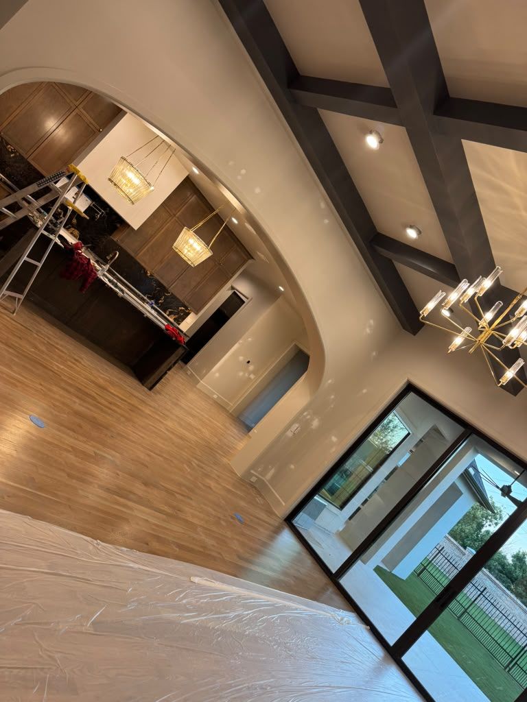 Modern lobby with wood floors, arched reception desk, chandeliers, and glass doors to a green outdoor area