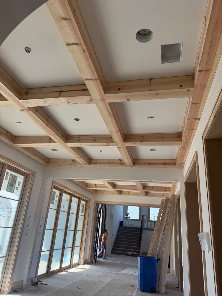 Interior hallway under construction with exposed wood framing and drywall, blue bin on the floor, and stairs ahead