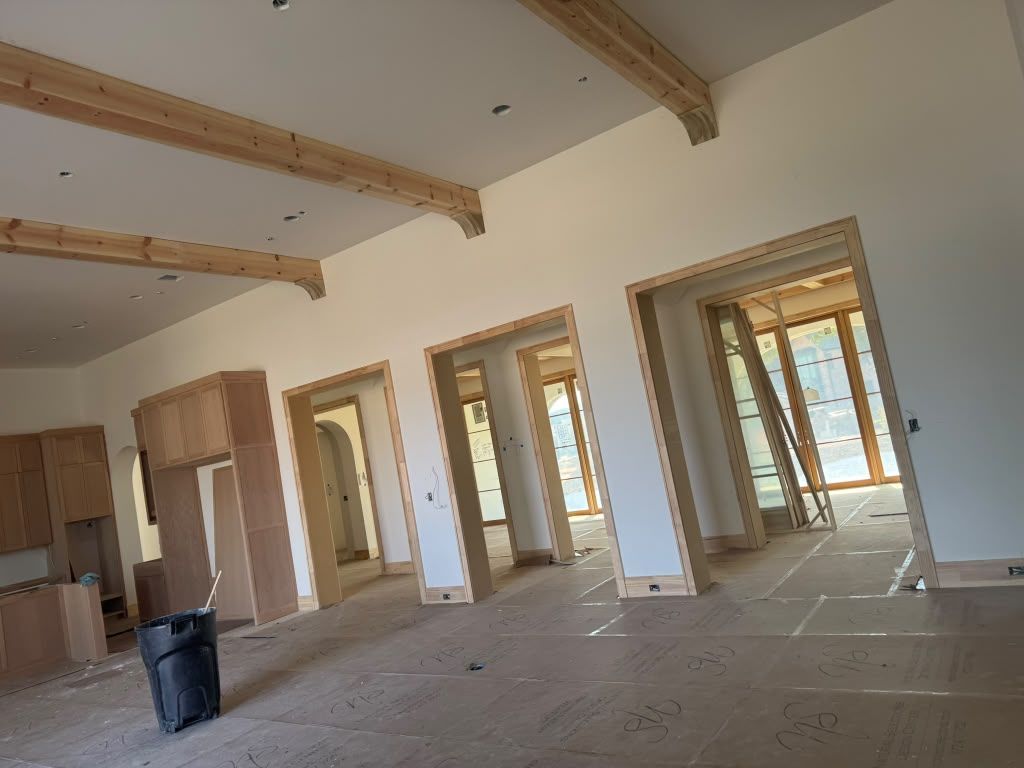 Empty unfinished room with exposed wooden ceiling beams, doorways, and construction materials on the floor