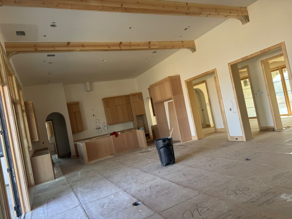 Unfinished living room with exposed beams, kitchen area, and open doorways leading outside.